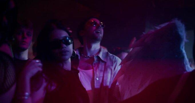 Stylish Man Dancing on a Dancefloor Under Colorful Flashing Lights in a Modern Nightclub. Male in Sunglasses Moving to Music Together with Excited Party Crowd. Low Angle Dynamic Portrait Shot