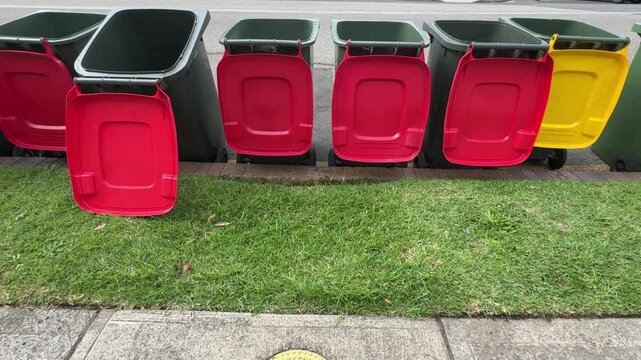 empty wheelie bins with lids flapping, in a row outdoors on a street in front of grass curbside in Sydney, Australia