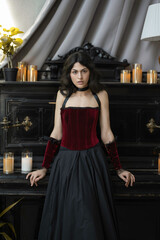Sensual dark haired girl in red vintage corset near piano with candles