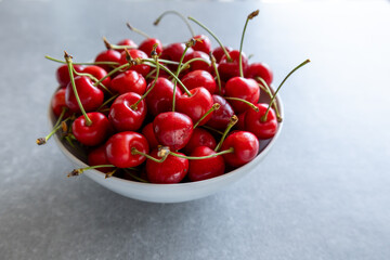 fresh red cherries in a white bowl on gray background, side view