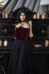 Sensual dark haired girl in red vintage velvet corset near piano with candles