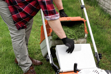 Gardener man in casual clothes carries plastic lawn mower box with cut grass of modern gasoline...