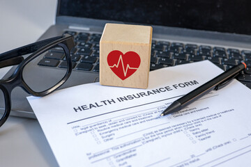 Health insurance policy. Health insurance form, red heart beat icon on wooden cube and computer on...