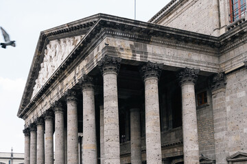 Close-up view of the neoclassical façade and Corinthian columns of the Degollado Theater in Guadalajara, Mexico, with a flying pigeon and detailed stone carvings