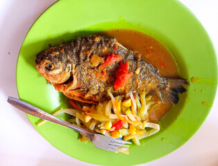Indonesian dish, fried pomfret fish with turmeric sauce, stir-fried chayote squash and corn on a green plate isolated on white background. Healthy food concept.