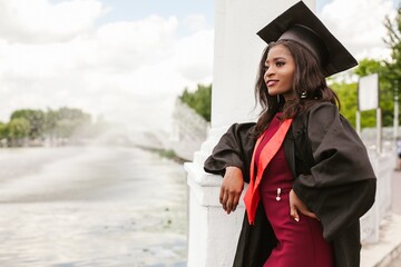 Young graduate leaning on a wall by a fountain wearing cap and gown