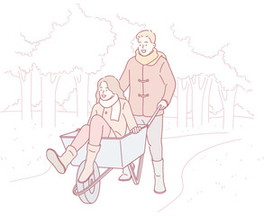 A couple enjoys a lighthearted and playful moment in a wheelbarrow surrounded by a serene park setting