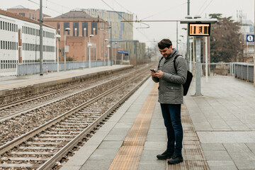 Man waits on train platform while using mobile phone in foggy weather