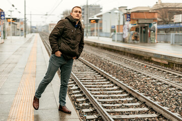 Man standing near train tracks at urban station during overcast day