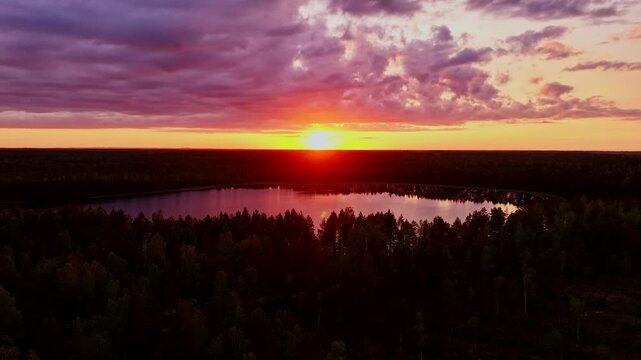 Colorful pink, orange clouds reflect on forest lake, drone lowers in Kemeri Park