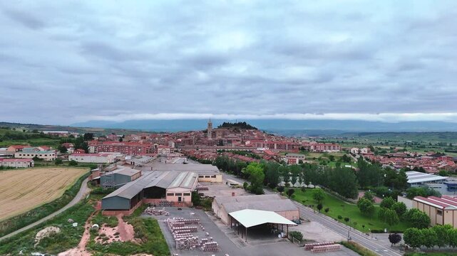 Forward aerial view of Navarrete village, La Rioja, Spain. Scenic townscape with church, rooftops, vineyards and hills under cloudy sky