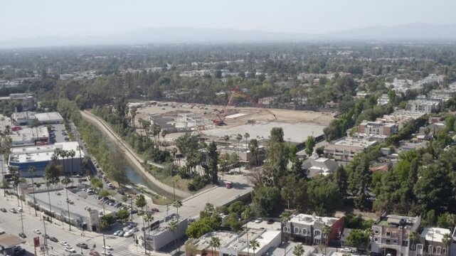 4K aerial of ambulance leaving large construction site with lights and sirens.
