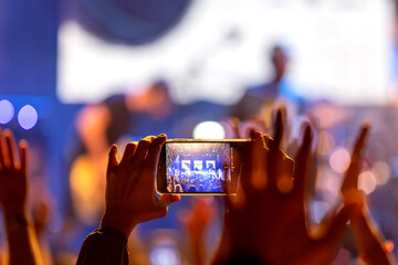 The audience records videos and takes photos with their smartphones during the concert of the musical band that performs on stage.