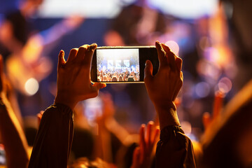 The audience records videos and takes photos with their smartphones during the concert of the musical band that performs on stage.