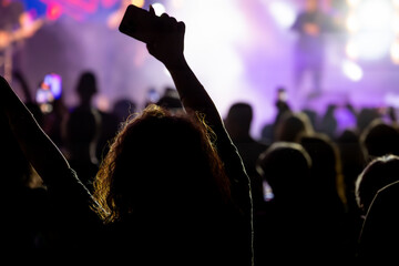 The audience gets excited and cheers with their arms raised during the concert of the musical band that performs on stage.