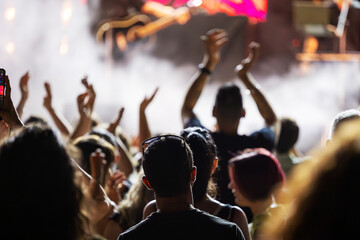 The audience gets excited and cheers with their arms raised during the concert of the musical band that performs on stage.