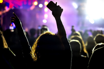 The audience gets excited and cheers with their arms raised during the concert of the musical band that performs on stage.