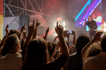 The audience gets excited and cheers with their arms raised during the concert of the musical band that performs on stage.