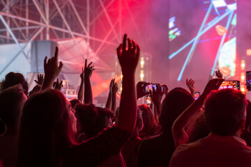The audience gets excited and cheers with their arms raised during the concert of the musical band that performs on stage.