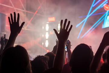 The audience gets excited and cheers with their arms raised during the concert of the musical band that performs on stage.