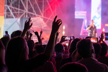 The audience gets excited and cheers with their arms raised during the concert of the musical band that performs on stage.
