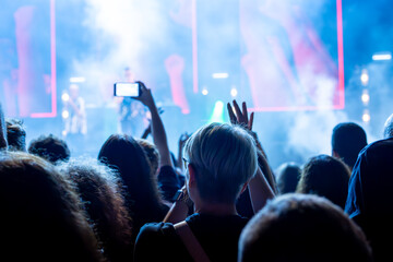 The audience records videos and takes photos with their smartphones during the concert of the musical band that performs on stage.