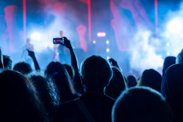 The audience records videos and takes photos with their smartphones during the concert of the musical band that performs on stage.