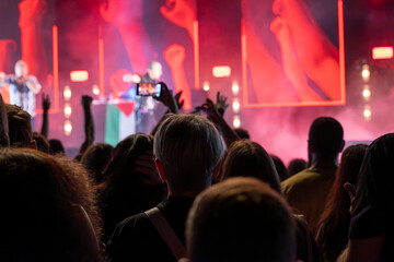 The audience records videos and takes photos with their smartphones during the concert of the musical band that performs on stage.