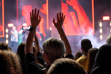 The audience gets excited and cheers with their arms raised during the concert of the musical band that performs on stage.