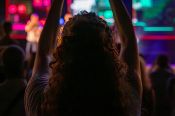 The audience gets excited and cheers with their arms raised during the concert of the musical band that performs on stage.
