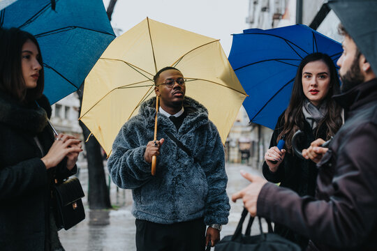 A group of four individuals having a discussion outdoors under colorful umbrellas during a rainy day. The atmosphere reflects collaboration, interaction, and planning amidst urban surroundings.