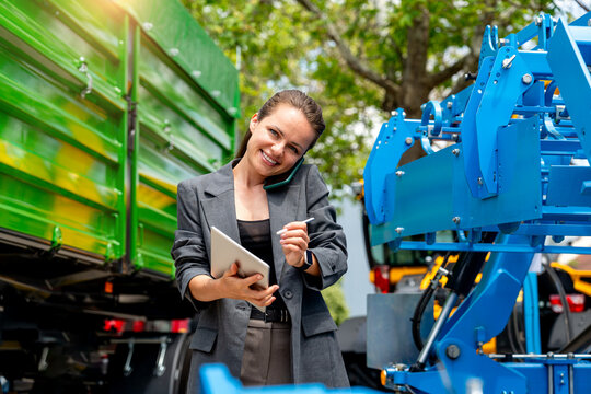 Professional woman in suit multitasking with phone and tablet near farm trailer at agricultural dealership - Powered by Adobe