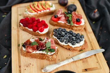 Bruschetta with labneh, prosciutto, salami, figs, peaches, cherry tomatoes, basil, and fresh berries. Rustic Italian-style appetizers with creative toppings