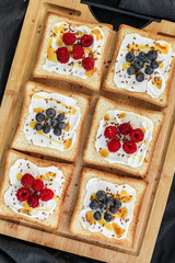 Flat lay of toasted white bread topped with labneh, fresh raspberries, blueberries, maple syrup, and flax seeds. Sweet breakfast or brunch idea with natural light and food styling