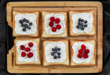 Flat lay of toasted white bread topped with labneh, fresh raspberries, blueberries, maple syrup, and flax seeds. Sweet breakfast or brunch idea with natural light and food styling
