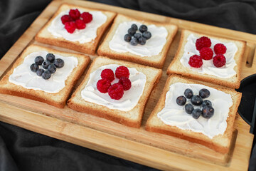Flat lay of toasted white bread topped with labneh, fresh raspberries, blueberries, maple syrup, and flax seeds. Sweet breakfast or brunch idea with natural light and food styling