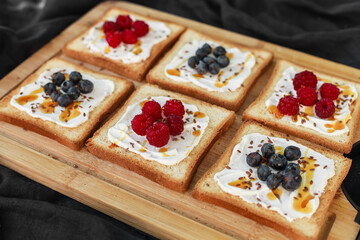 Flat lay of toasted white bread topped with labneh, fresh raspberries, blueberries, maple syrup, and flax seeds. Sweet breakfast or brunch idea with natural light and food styling