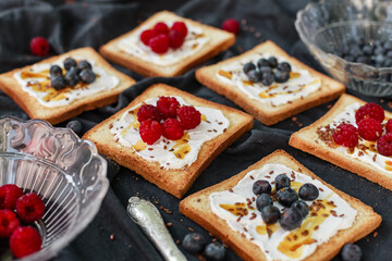 Flat lay of toasted white bread topped with labneh, fresh raspberries, blueberries, maple syrup, and flax seeds. Sweet breakfast or brunch idea with natural light and food styling