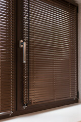 Closed wooden blinds 25 mm close-up on the window, casting subtle lines of light and shadow. The sleek handle and warm wood tones add a touch of modern privacy and interior design elegance.