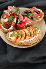 Bruschetta with labneh, prosciutto, salami, figs, peaches, cherry tomatoes, basil, and fresh berries. Rustic Italian-style appetizers with creative toppings