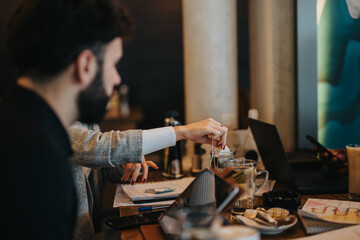 Two individuals are seen discussing work in a cafe, with laptops and documents, showcasing collaboration and teamwork in a casual atmosphere.