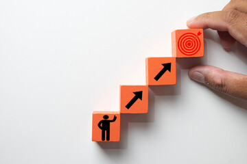 Hand arranging wooden blocks in steps, from a person icon to a target goal. Concept for business growth, career path development, achieving objectives,personal development, ambition, self-improvement.