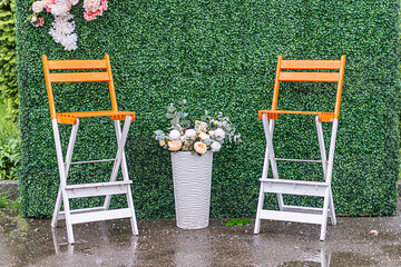 Two orange stools with white legs, flanked by a striped metal vase holding a large bouquet of...