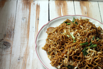 Plate of stir-fried noodles with vegetables served on a rustic wooden table, in soft natural lighting. Asian comfort food concept.
