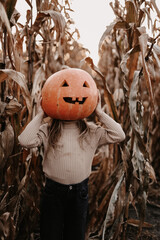 Happy Halloween. Little child girl with big pumpkin head having fun outdoors at autumn dry corn field. Children's party with jack-o-lantern, trick or treat. Festive carnival