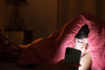 Sleep-deprived woman in bed illuminated by screen light, showing impact of screens on rest.