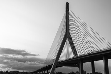 Obraz premium Black and white view of the Flintshire Bridge, highlighting its dramatic concrete pylon and radiating cables against a cloudy sky