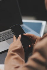 Young beautiful Asian businesswoman holding smartphone while working in the office room.