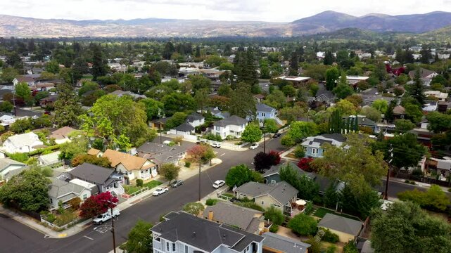 Drone flies above nearby town adjacent to Napa with tree lined streets, orbit under overcast sky