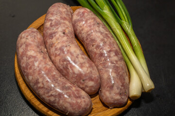 Meat sausages with garlic and green onions, prepared for grill, on a wooden board. Raw sausages for grill.